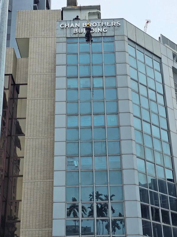 Rope access technician repairing high-level façade signage on Chan Brothers Building in Singapore